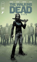 Comic book cover of 'The Walking Dead' with a character holding a weapon and a group of survivors in the background.