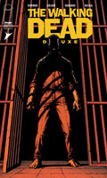 Comic book cover of 'The Walking Dead Deluxe' with a silhouette of a character in front of bars.